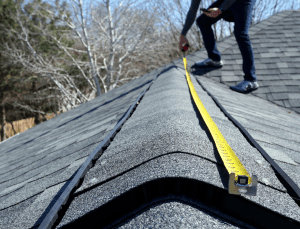 A roofing contractor measures a home roof with a measuring tape.